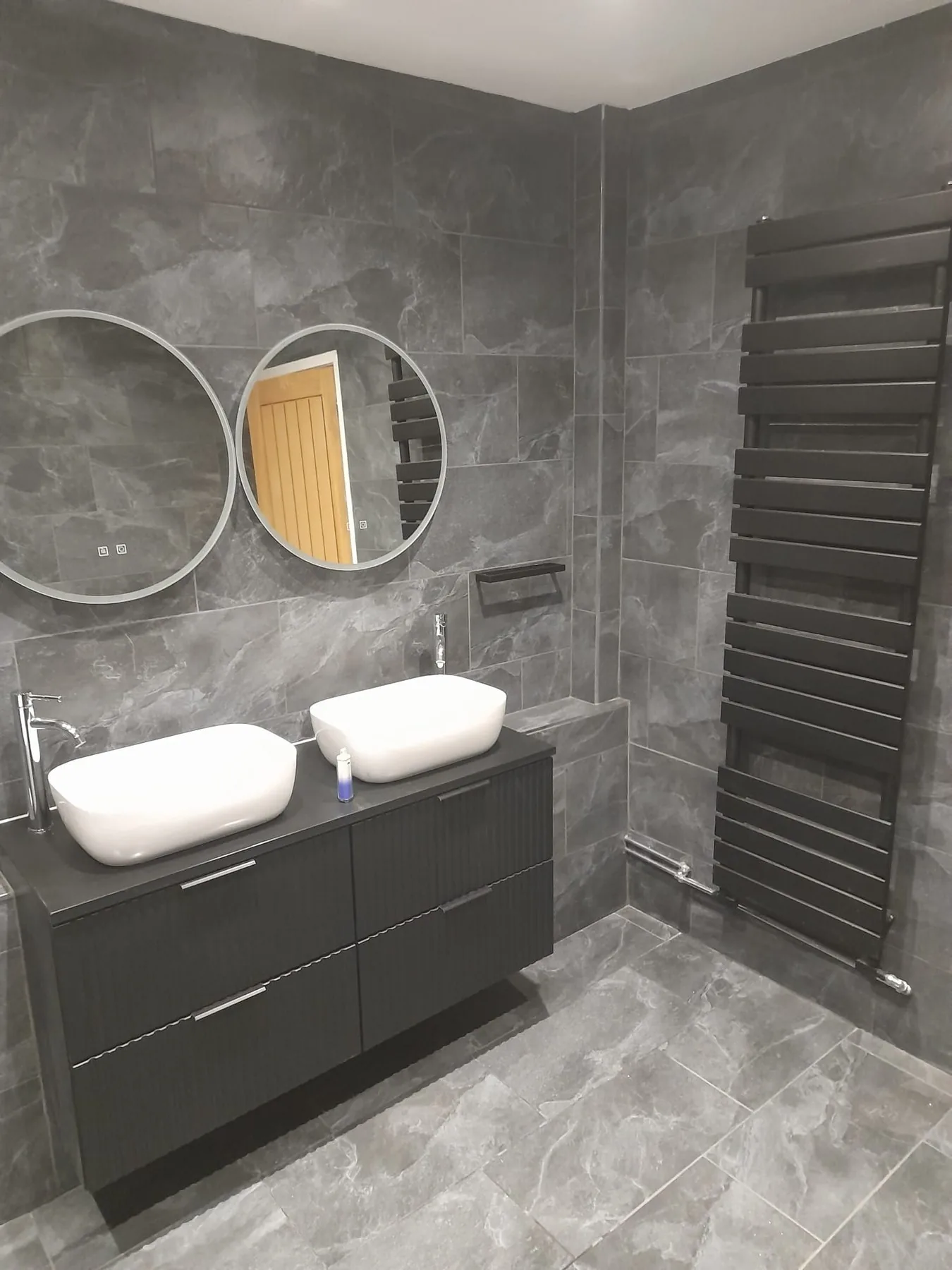 Completed dark tiled bathroom with double basins by Campbell and Sons